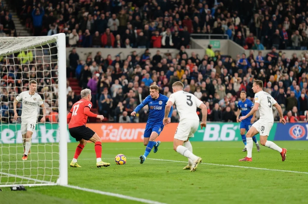 足球场上新老球员正在配合比赛，画面展现激烈对抗与团队协作，观众席上气氛热烈